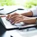 Close up hand of female typing on keyboard of laptop on table, working with technology device in modern office